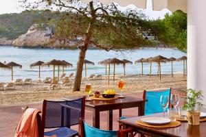 a table and chairs on a beach with umbrellas at Meliá Cala Galdana in Cala Galdana