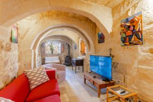 a living room with a red couch and a tv at Bebbuxija Pool Farmhouse Gozo - Happy Rentals in Xagħra