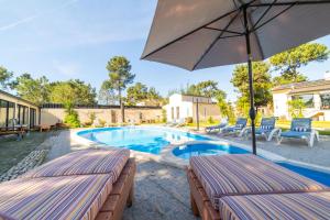 - une piscine avec 2 chaises longues et un parasol dans l'établissement Villa Praia e Floresta, à Aroeira