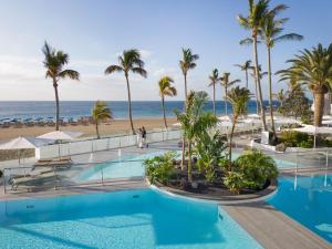 a pool at the beach with palm trees and the ocean at Plus Fariones Suite Hotel in Puerto del Carmen