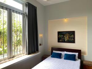 a bedroom with a bed with blue pillows and a window at Phòng VIP Xông Hơi View hồ bơi in Ấp Phú Khương