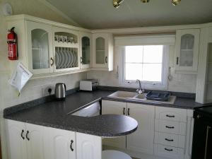 eine Küche mit weißen Schränken und einer schwarzen Arbeitsplatte in der Unterkunft The Wolds Vogue II 6 Berth Central Heated in Ingoldmells