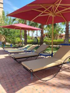 a row of lounge chairs with red umbrellas at Villa Rosa - Iconic Riad on 2 hectares of privacy in El Aggada