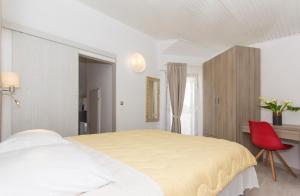 a white bedroom with a bed and a red chair at Alison Apartments in Premantura