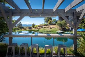 eine Gruppe von Hockern unter einer Pergola mit Blick auf einen Teich in der Unterkunft Mariri Heights Sequoia Cottage in Lower Moutere