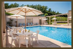 uma piscina com mesas e cadeiras e um guarda-sol em Farina Park Hotel em Bento Gonçalves