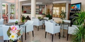 a restaurant with tables and white chairs and plants at Hotel City in Misano Adriatico
