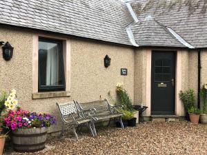 a bench sitting in front of a house with flowers at Garden Bank Cottage in Kelso