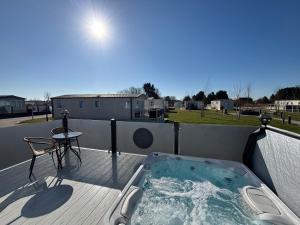 a hot tub on a deck with a table and a chair at The Retreat 10 - Hot tub Mini Lodge, central heating, bed linen, & pet friendly - Meadow Lakes Caravan Hire in Chapel Saint Leonards
