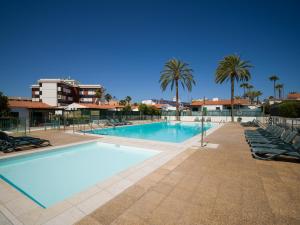 a large swimming pool with chairs and palm trees at Refurbished 2 bedrooms house private pool in San Bartolomé de Tirajana