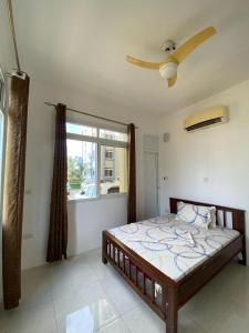 a bedroom with a bed with a ceiling fan and a window at Zanzibar Manolo Apartment in Zanzibar City
