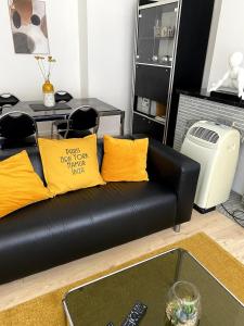 a black leather couch with yellow pillows in a living room at Appartement lumineux, idéalement situé - Enfants bienvenus in Namur