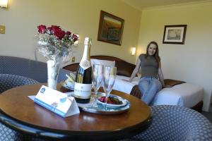 una donna seduta su un letto in una stanza d'albergo con una bottiglia di champagne di Alpine Motor Inn a Katoomba