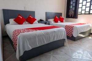 two beds with red pillows in a room at Hotel Puerta Sur in Comitán