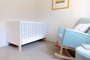 a baby room with a crib and a chair at Banksia House Cape Paterson in Cape Paterson
