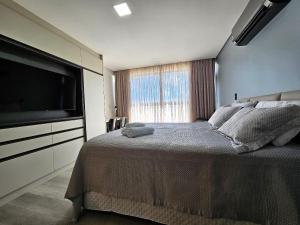 a bedroom with a large bed and a large television at Studio espaçoso e confortável a 50m da praia in Tambaú