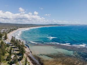 Merduka Sands 4 - Cozy charming cottage في Brooms Head: اطلالة جوية على شاطئ به اشجار والمحيط