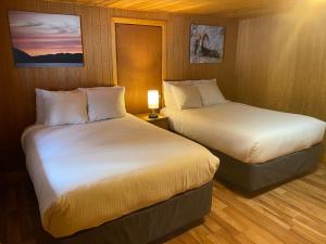 two beds in a hotel room with a lamp at Double G Service in Muncho Lake