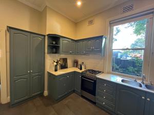 d'une cuisine avec des placards verts, un évier et une fenêtre. dans l'établissement Kelpie Cottage, Luxe 1930s Stay in the Heart, à Albury