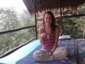 una ragazza seduta su un letto con una tazza di caffè di WOOD CABIN LODGE IN THE FOREST book here treking with us a Bukit Lawang Altre 68 foto