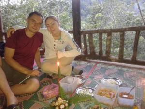un uomo e una donna seduti su un tavolo con una candela di WOOD CABIN LODGE IN THE FOREST book here treking with us a Bukit Lawang