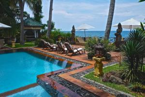 a swimming pool next to chairs and the ocean at Villa Boreh Beach Resort and Spa in Tejakula