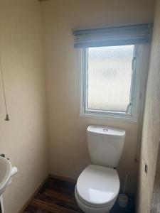 a bathroom with a white toilet and a window at 6 Bed Static Carvan Seawick Holiday Park in Saint Osyth