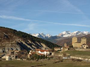 un pueblo en una colina con montañas nevadas en el fondo en El Churrón, en Larrés