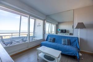 a living room with a blue couch and a large window at Les Marinas front of the beach in Courseulles-sur-Mer