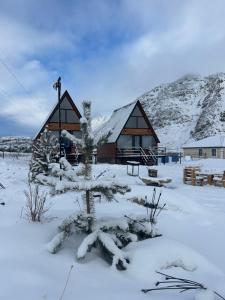 a cabin in the snow with a tree in the foreground at MTISGULI Cottages in Stepantsminda