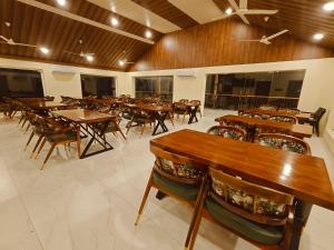 Un gran comedor con mesas y sillas de madera. en Aldea Retreat Resort, en Kūvattūr