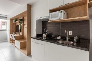 a white kitchen with a sink and a microwave at Apartamento completo localizado em um dos melhores bairros de Porto Alegre. in Auxiliadora