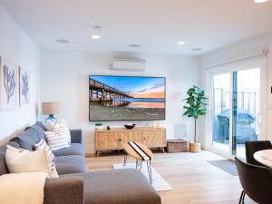 a living room with a couch and a tv on a wall at 2026 Award Winner, Luxe 2BR, steps to sand & pier, with fire pit, AC and parking in Newport Beach