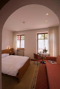 Schlafzimmer mit einem Bett, einem Tisch und Fenstern in der Unterkunft Hotel Waldheim Belvedere in Brixen