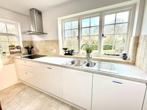 eine Küche mit weißen Schränken und einer Spüle und Fenstern in der Unterkunft Swan Cottage 2-Bedroom-Netflix-Parking-Nature-Canal in Kidlington