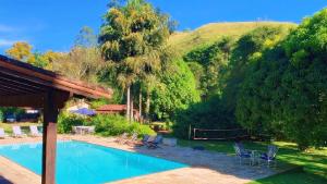 a swimming pool with chairs and a hill in the background at Recanto da Paz Tur - Relax e charme na serra in Miguel Pereira