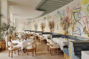a restaurant with white tables and chairs and a colorful wall at The Maybourne Beverly Hills, Maybourne in Los Angeles