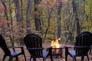three chairs around a camp fire in the woods at Secluded Retreat w Hot Tub, FirePit & Pool Access in Hedgesville