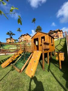a wooden playground with a play house on the grass at Bangalô com 3 suítes no Eco Resort na Praia dos Carneiros in Tamandaré