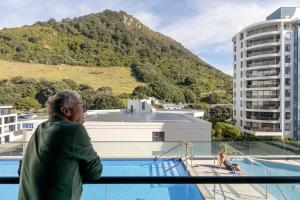 a man standing on a balcony looking at a mountain at Spectacular Sunrises & Sea Views - Pool Spa Gym in Mount Maunganui