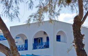 a white building with blue windows and trees at Rodothea and Adams on the Beach, Santorini in Monolithos