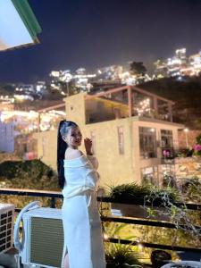 a woman in a white dress standing on a balcony at night at Vạc Villa - Tam Đảo Retreat in Tam Ðảo