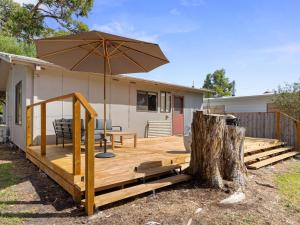 a wooden deck with an umbrella next to a house at Little Pier Cottage in Inverloch