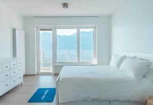 ein weißes Schlafzimmer mit einem großen Bett und einem großen Fenster in der Unterkunft Duplex Lakeside Penthouse in Porto Valtravaglia