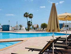 a pool with chairs and an umbrella next to a swimming pool at Canaryislandshost I Dalia in Puerto del Carmen