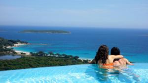 a man and woman sitting in a infinity pool overlooking the ocean at Résidence Belvedere de Palombaggia in Porto-Vecchio