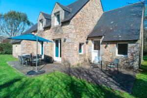 une maison en pierre avec une table, des chaises et un parasol dans l'établissement Kerlavarec - Belle maison avec grand jardin, à Locmariaquer