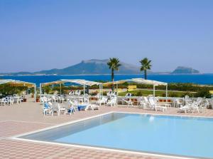 a pool with chairs and umbrellas and the ocean at Hotiday Golfo Aranci in Golfo Aranci