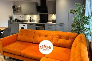 an orange couch in a living room with a kitchen at FREE GATED PARKING - 2 bed Apartment - Holbeck Leeds in Beeston Hill
