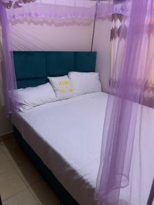 a bed with a purple canopy and white sheets and pillows at Angie's Nest in Syokimau